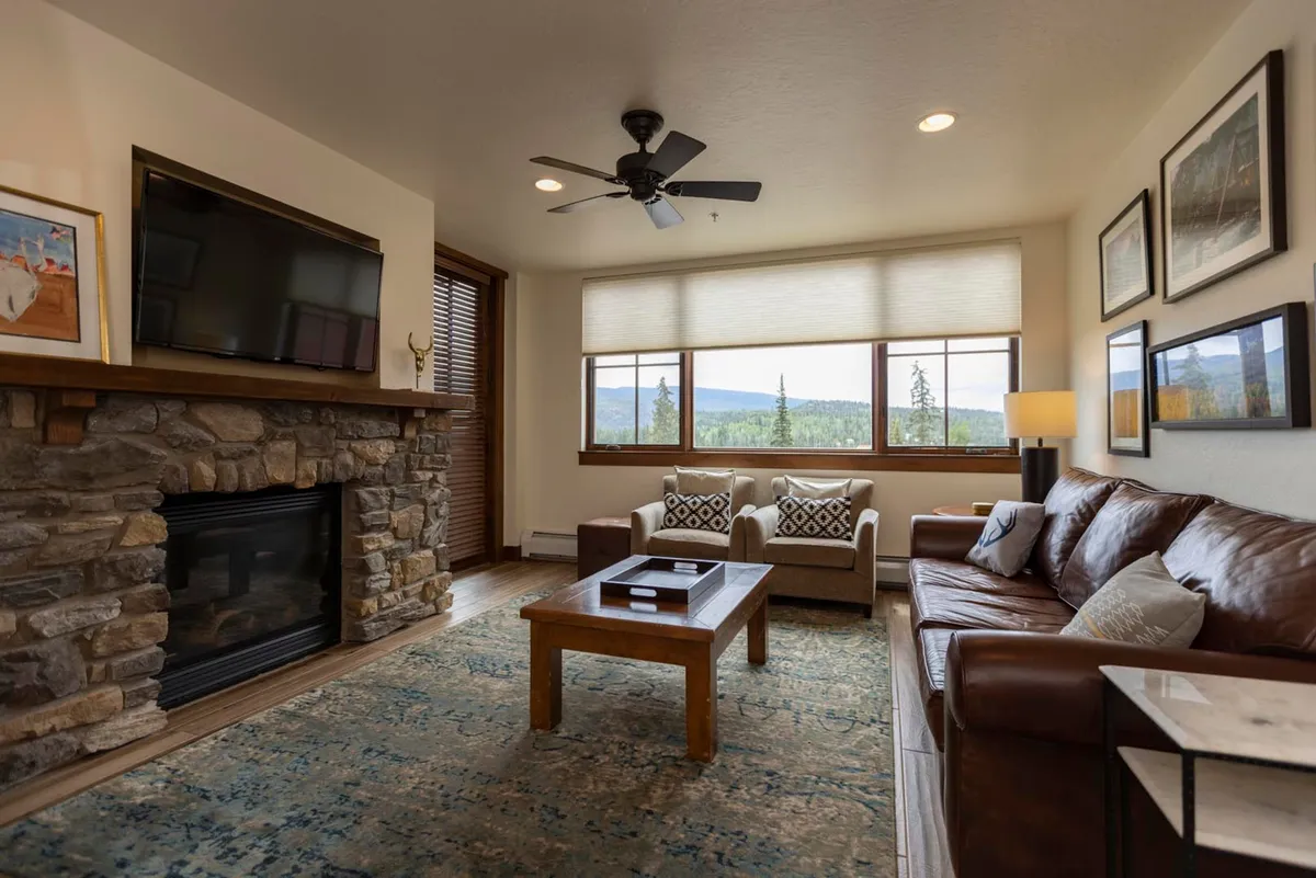 A welcoming lounge area with a grand stone fireplace, large windows framing mountain views, and plush seating. The cozy atmosphere is perfect for families to gather, relax, and enjoy time together after days filled with excitement.