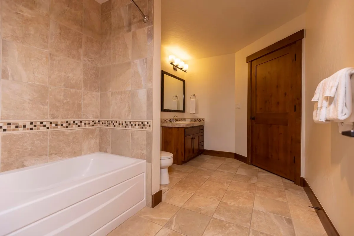 This image captures a tranquil and well-appointed bathroom featuring a bathtub and a vanity with a large mirror, framed by subtle wooden accents and a serene atmosphere. The setting suggests the possibility of soothing baths and moments of self-care, providing a retreat-like vibe within the lodge.