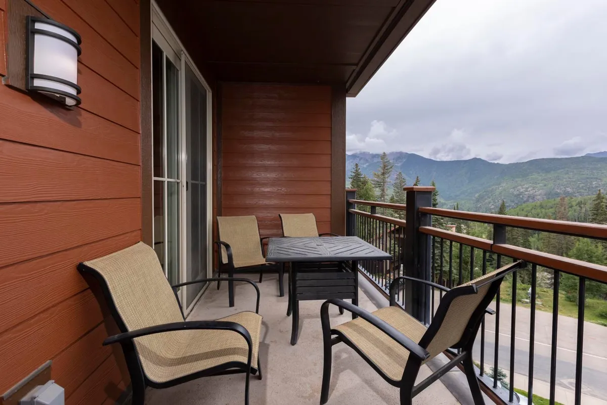 This serene image features a private balcony with comfortable seating and a small table, overlooking breathtaking mountain scenery. The view speaks to tranquil mornings, sunset reflections, and a seamless connection to the outdoors.