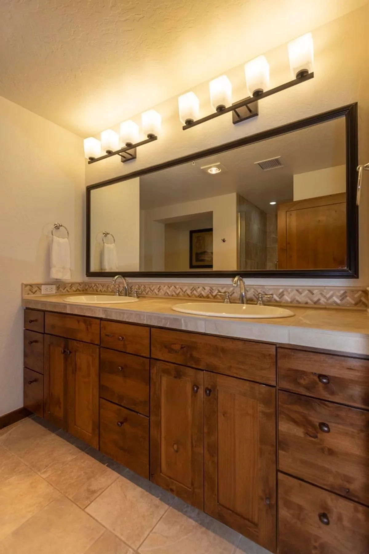 A serene bathroom with a double sink vanity, expansive mirror, warm wooden cabinetry, and elegant lighting. The mood is calm and soothing, ideal for unwinding after a day of adventure.