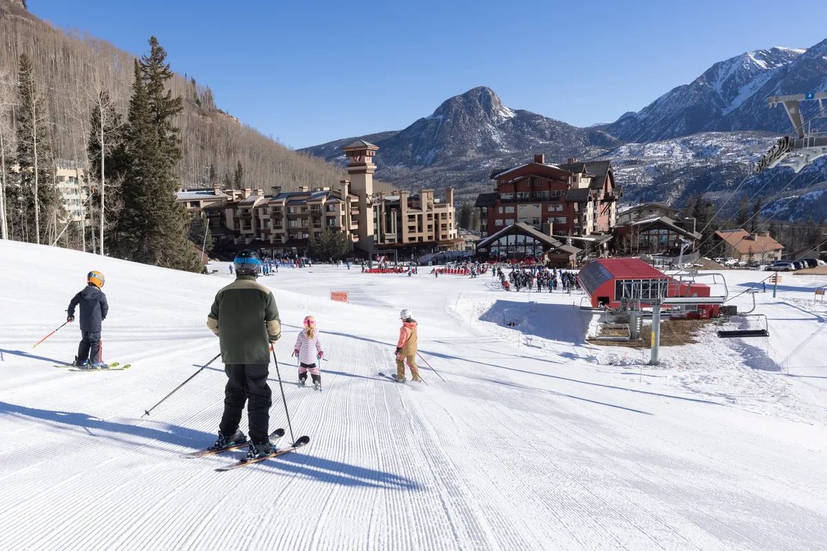 A lively scene of skiers enjoying the slopes with the lodge and ski lift in the background. The snowy landscape and active guests showcase the family-friendly, adventurous spirit of Purgatory Resort, while also emphasizing the proximity of the lodge to recreational activities.
