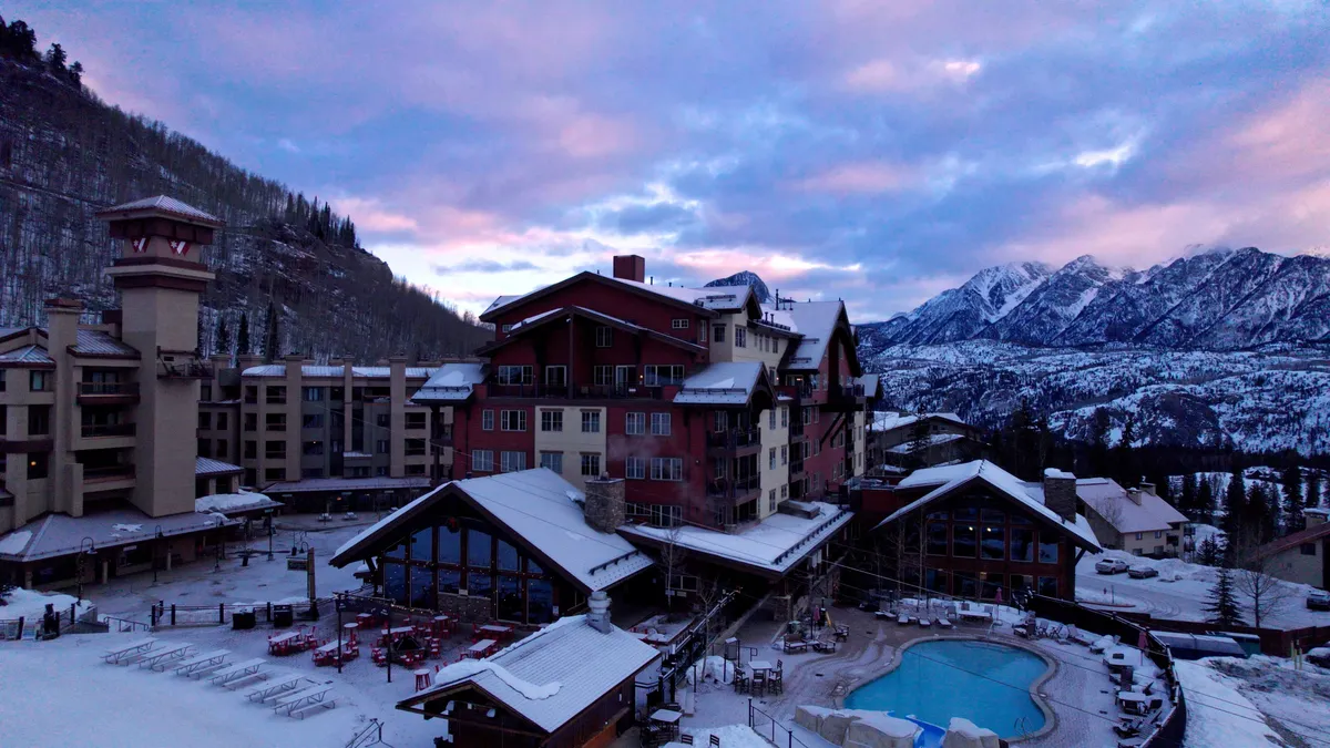 This image captures the hotel's outdoor pool area nestled against a breathtaking mountain backdrop. The scene highlights the inviting heated pool, outdoor seating, and the overall resort atmosphere. Snow-dusted surroundings emphasize the unique experience of swimming and relaxing outdoors even in colder weather.